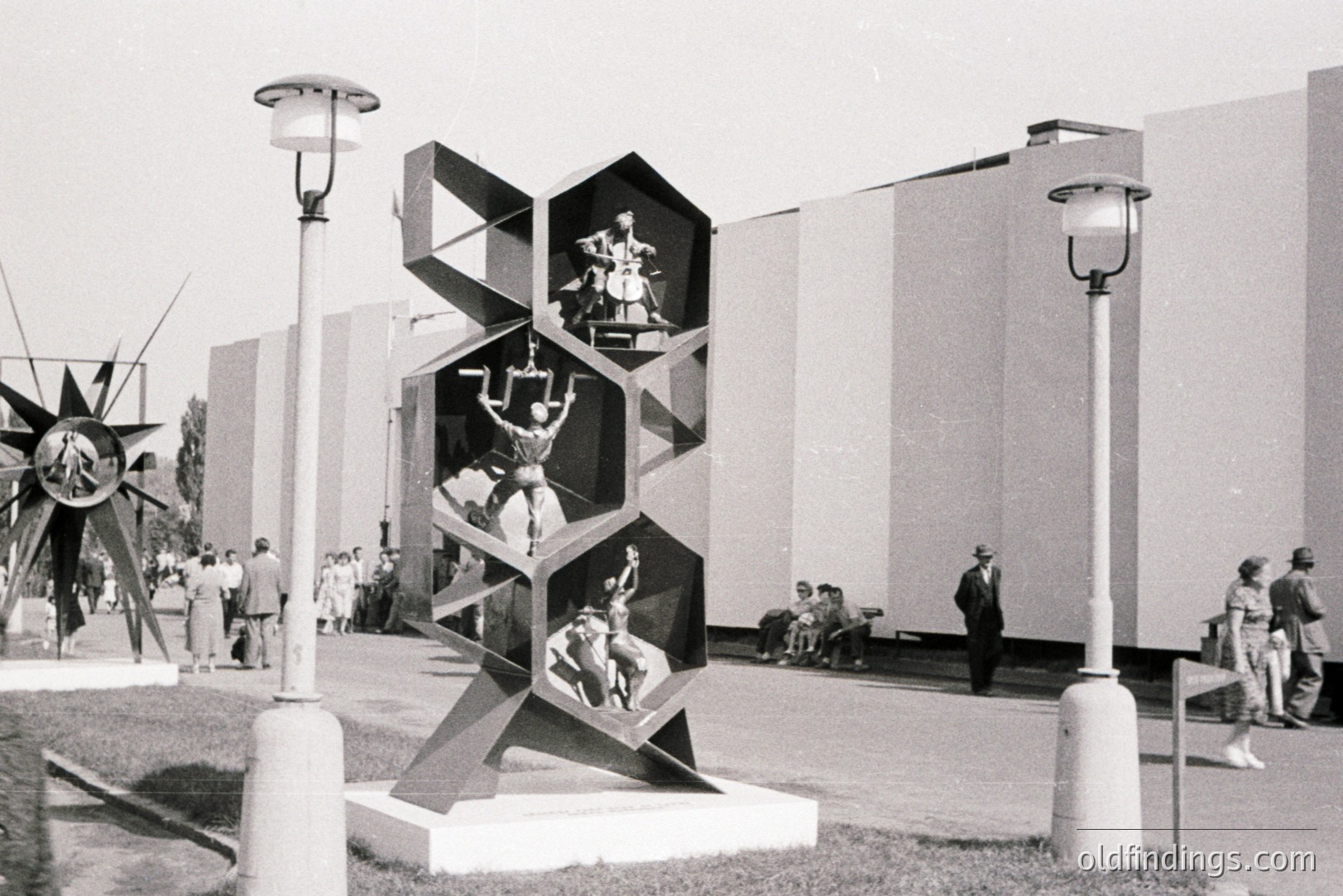 Geometric sculpture displaying figures in dynamic poses within hexagonal compartments. Likely an exhibition or public space; crowds observe. Architectural backdrop appears modernist, possibly concrete. Estimated 1960s, Eastern European context. Possible design reference or archival stock image.
