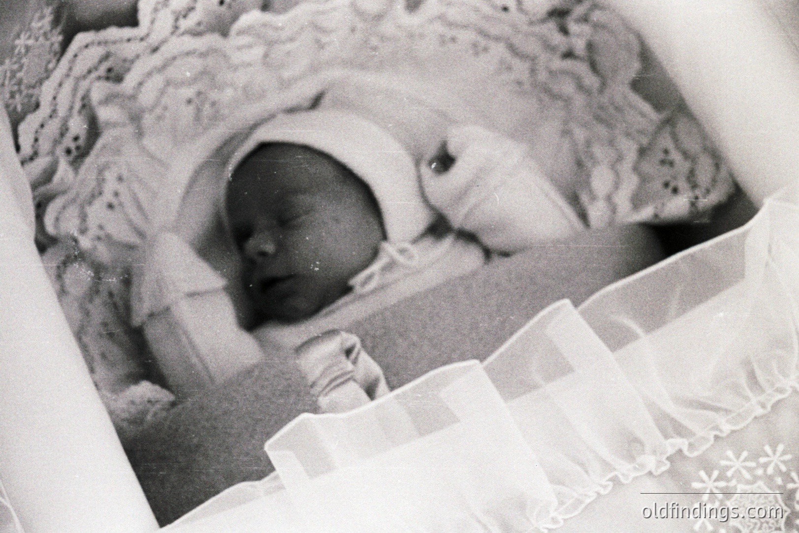 Infant sleeps peacefully in a lace-trimmed cot, swaddled in white cloth. The photograph's grain suggests a vintage print, likely from the mid-20th century. A sense of domesticity and fragility. Possible sentimental value for family archives.
