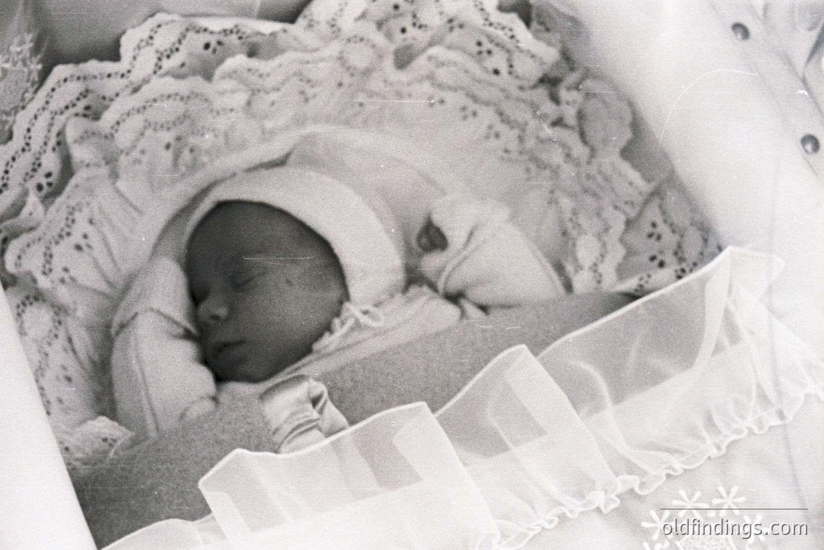 Close-up, black and white portrait of a sleeping infant, swaddled in delicate lace, suggesting a vintage or historical family photograph. The soft focus and grainy texture hint at an earlier photographic process. Likely a studio portrait, evoking nostalgia and representing early childhood.