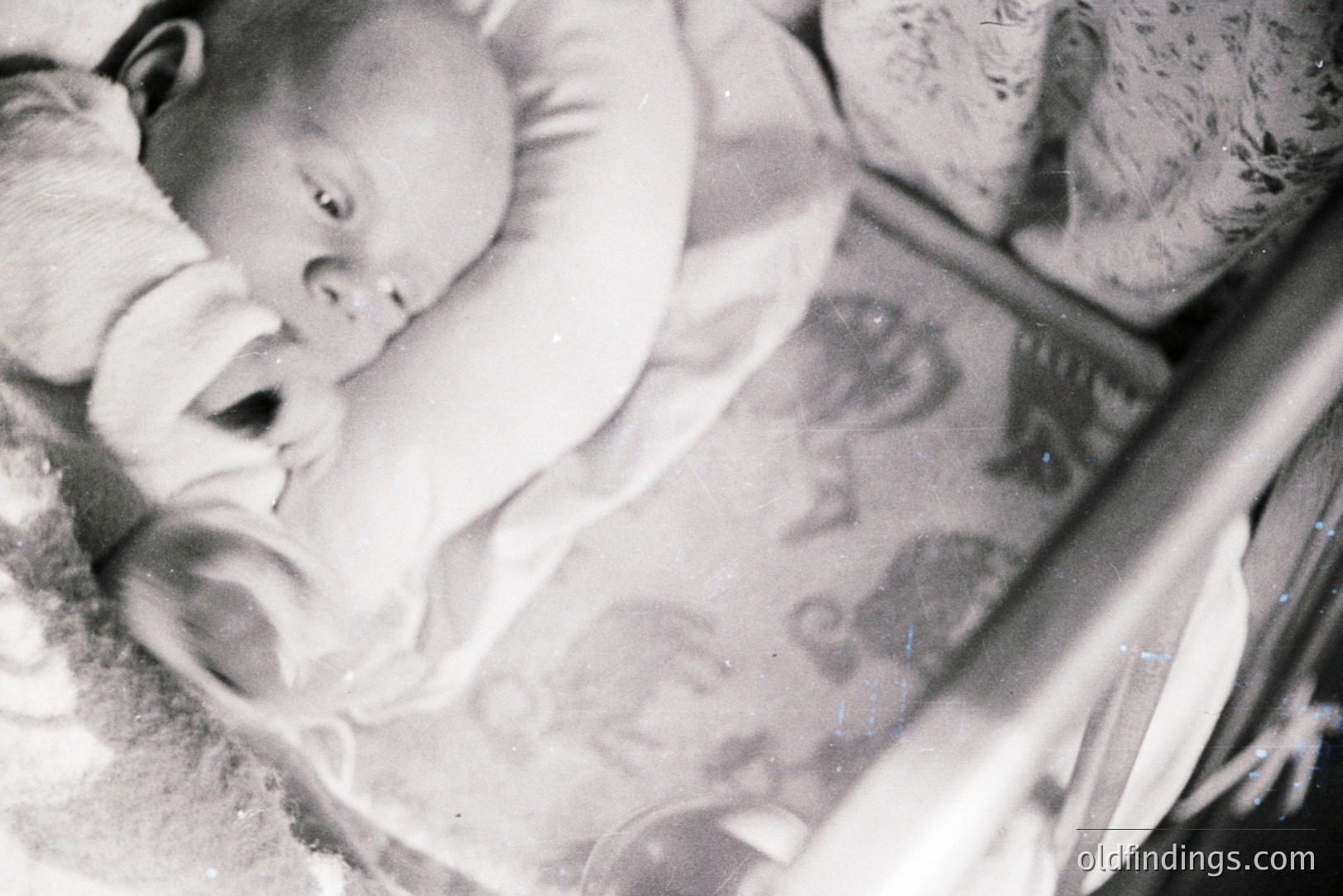 A baby lies peacefully in a vintage, wicker travel crib. Visible details include a patterned blanket and a soft headrest. The monochrome photography suggests a likely 1960s-1970s origin. Potential commercial use: baby product design, vintage lifestyle stock.