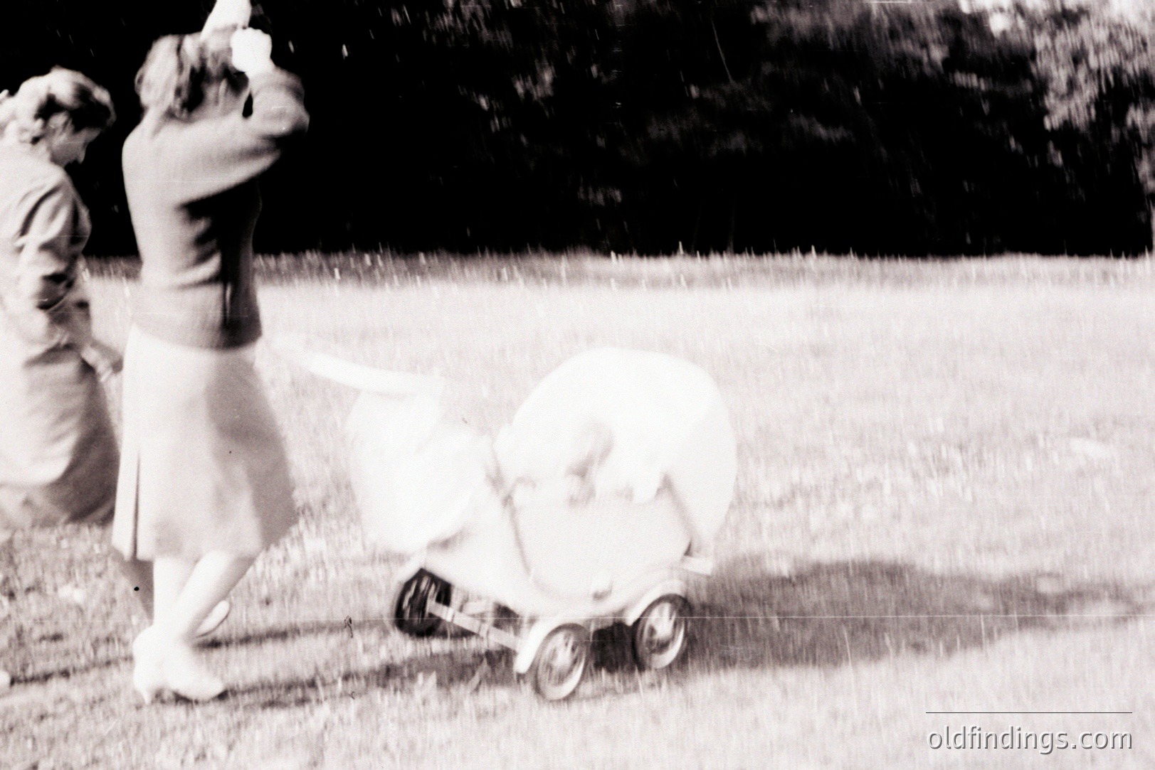 Vintage black and white shot captures a woman in a 1960s-style dress, pushing a vintage baby carriage across a grassy lawn. Details suggest a prosperous, mid-century lifestyle. The carriage’s design is indicative of the era. This image holds value as a historical representation of domesticity.