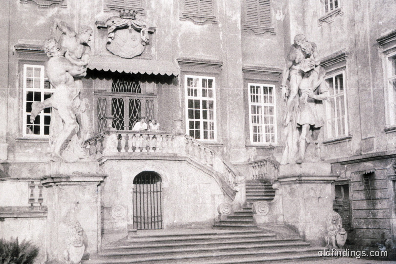 Ornate, monumental entrance showcasing classical sculpture & tiered steps. Architectural details suggest European influence, possibly late 19th/early 20th century. A single figure is visible on a balcony. Likely a stately home or institutional building.