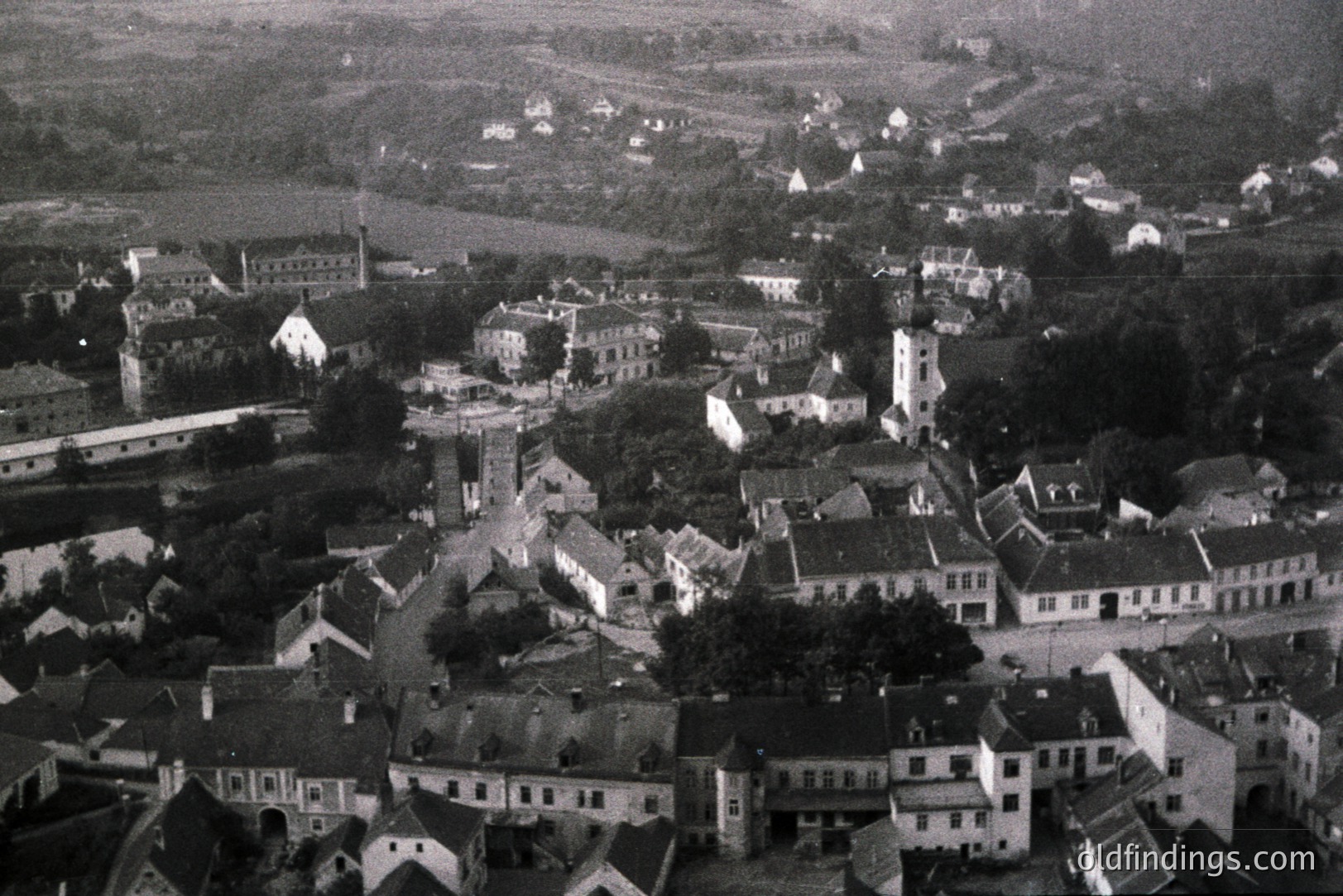 An aerial view captures a compact European town, showcasing tightly packed, gabled buildings and a central church steeple. The architecture suggests a historical, possibly rural, setting. Likely from the mid-20th century, this image offers insight into urban planning and regional life.