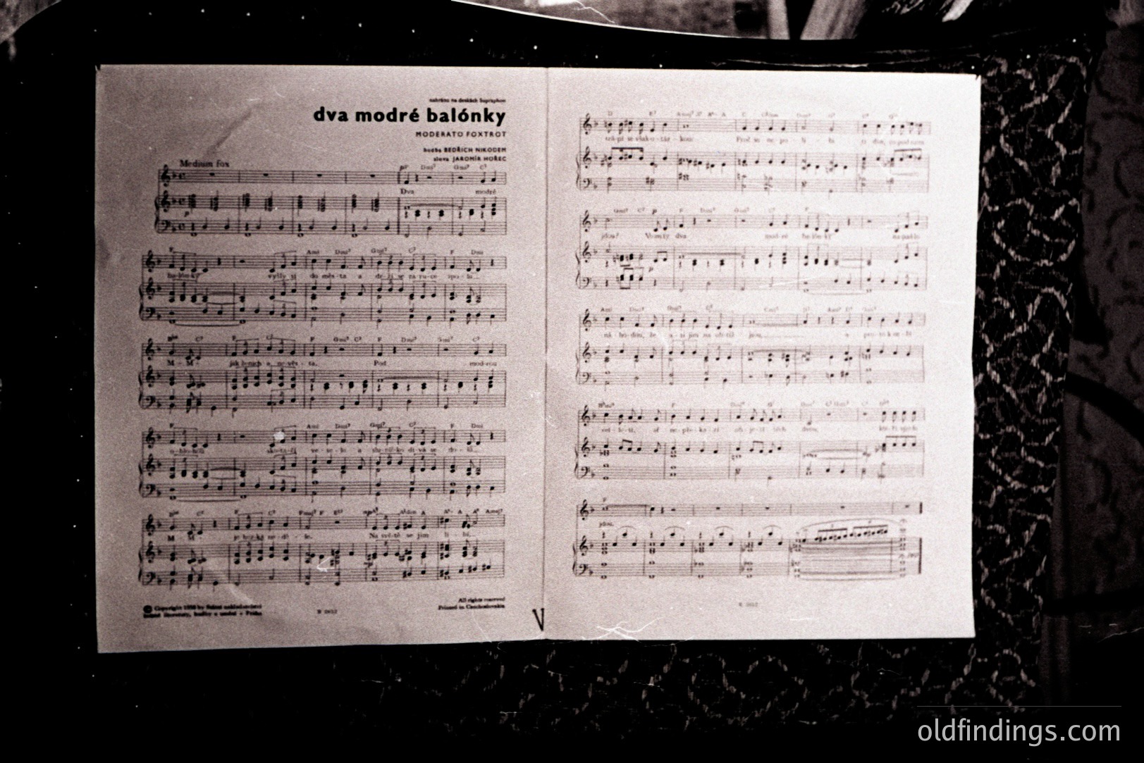 Sheet music titled "dva modré balónky" displayed on an ornate stand. The score features vocal and piano parts, displaying complex notation. Likely a vintage publication, possibly from the mid-20th century. Details of the stand's background suggest a domestic interior.