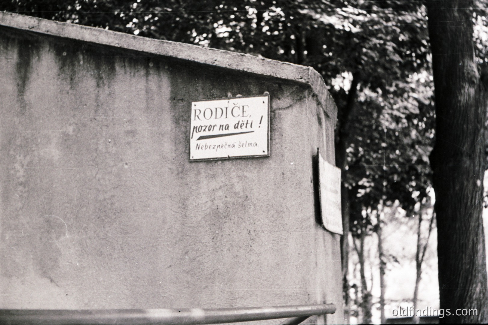Close-up of a weathered sign attached to a concrete wall. The text, in Cyrillic script, reads “Rodīče, pozor na děti!” and “Bezpečná zóna.” Likely a public safety warning for parents regarding children in a designated zone. Appears to be vintage photography, possibly 1970s or 80s. Location likely Eastern Europe.
