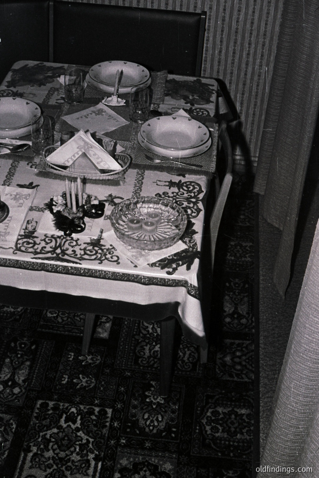 A formally set table features patterned linens, glassware, and floral arrangements. The dining area is illuminated by candlelight, suggesting a special occasion. Likely 1950s-1970s domestic interior, potentially used for stock photography or design reference. Evokes vintage hospitality and a cozy atmosphere.