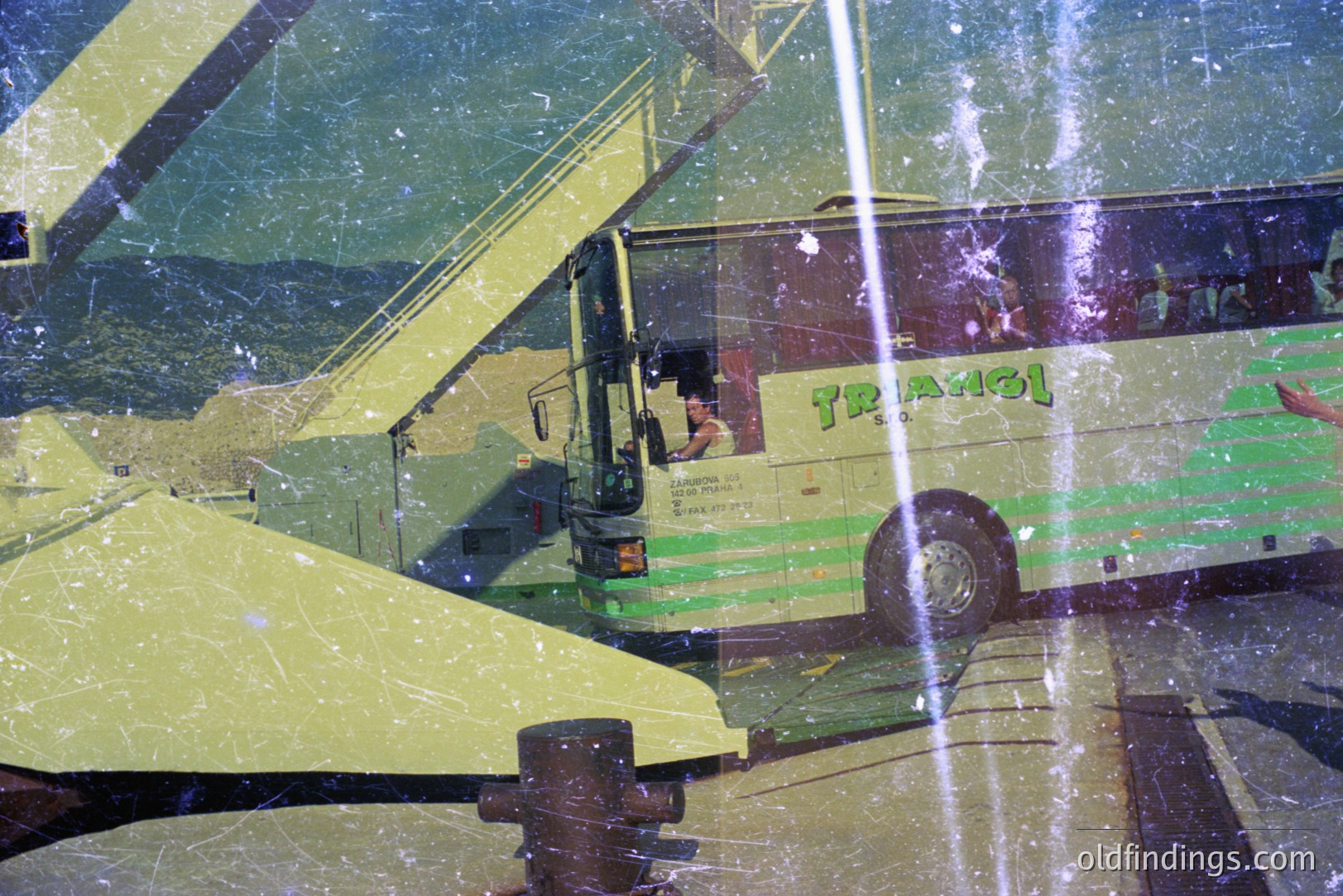 A green “Triangel” tour bus is parked amidst a blurred, sun-drenched landscape; a crane's boom overlaps the scene. Visible text on the bus suggests a Bulgarian origin. The photo’s grainy texture hints at a vintage film aesthetic, potentially the 1970s. Commercial value: potentially stock for travel or retro design.