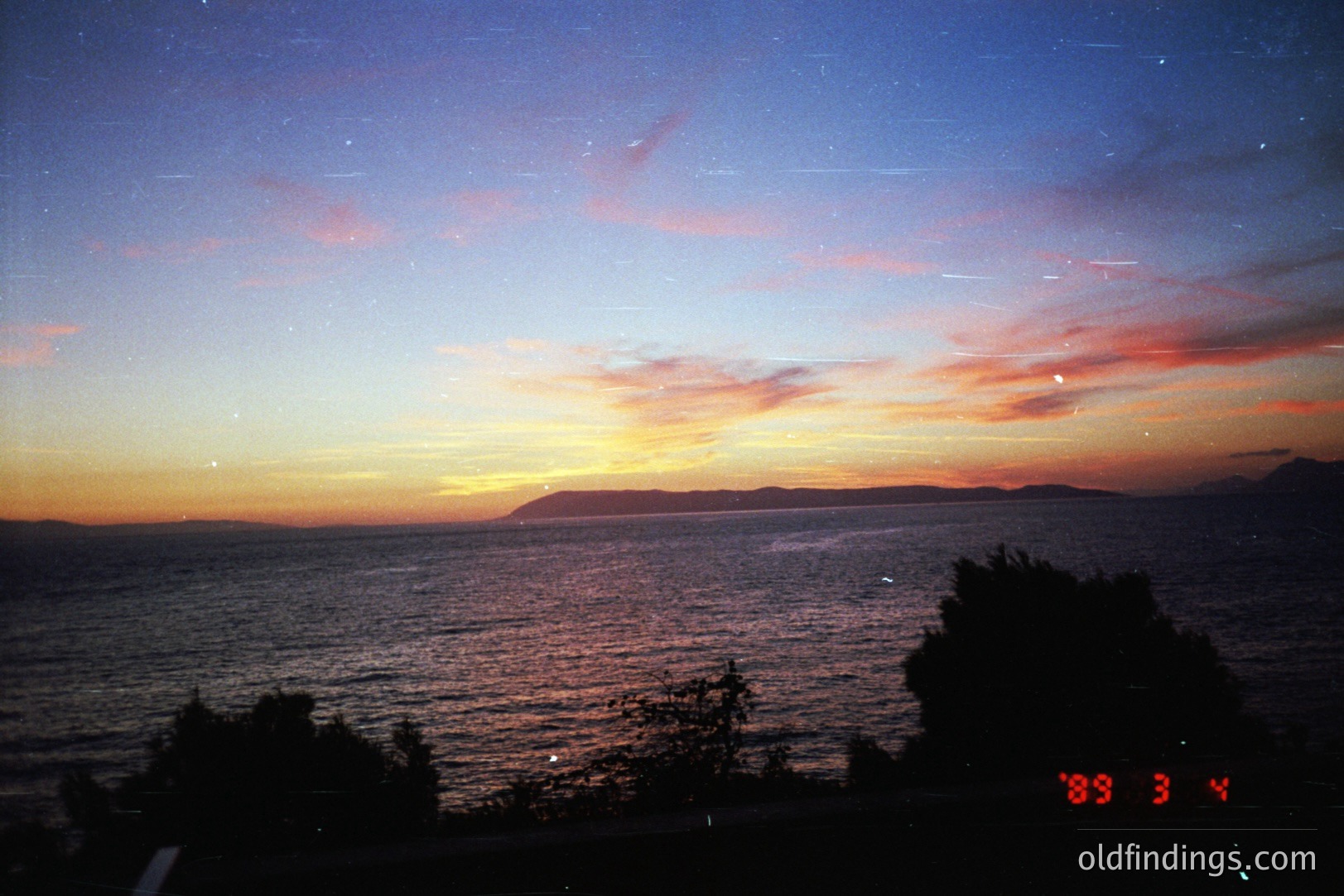 Vivid sunset over a body of water, possibly the Black Sea. Silhouetted trees frame the view of the orange and red sky reflecting on the water's surface. Appears to be a coastal scene with a distant landmass. Likely captured on film, showing slight grain.