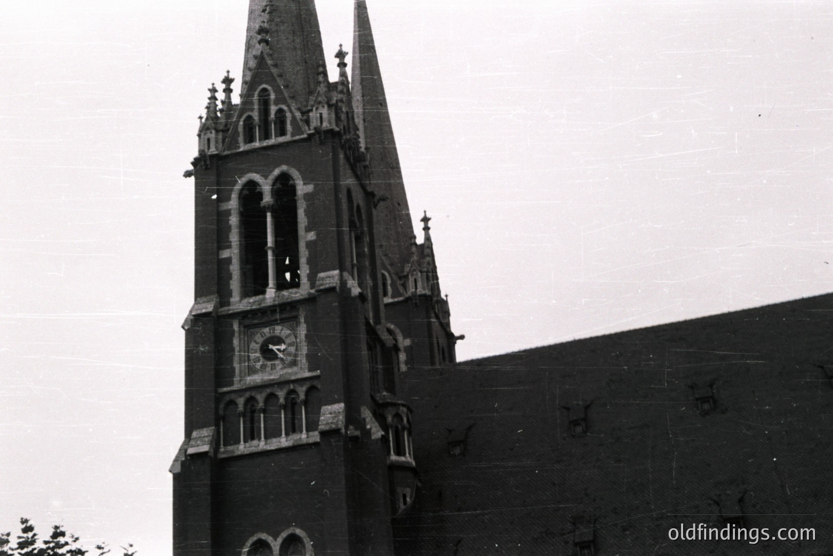 Ornate, dark brick church tower with pointed spire and clock face. Gothic Revival architecture featuring detailed tracery and stone accents. Likely a regional church, possibly late 19th or early 20th century. The image exhibits vintage wear & grain.