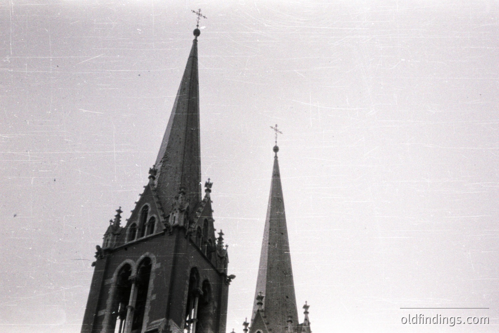 Dramatic, high-angle view of two Gothic spires reaching skyward. Detailed tracery and pointed arches are visible. Likely a cathedral or significant church. Appears to be an architectural study or older postcard image. Distressed paper texture suggests age.