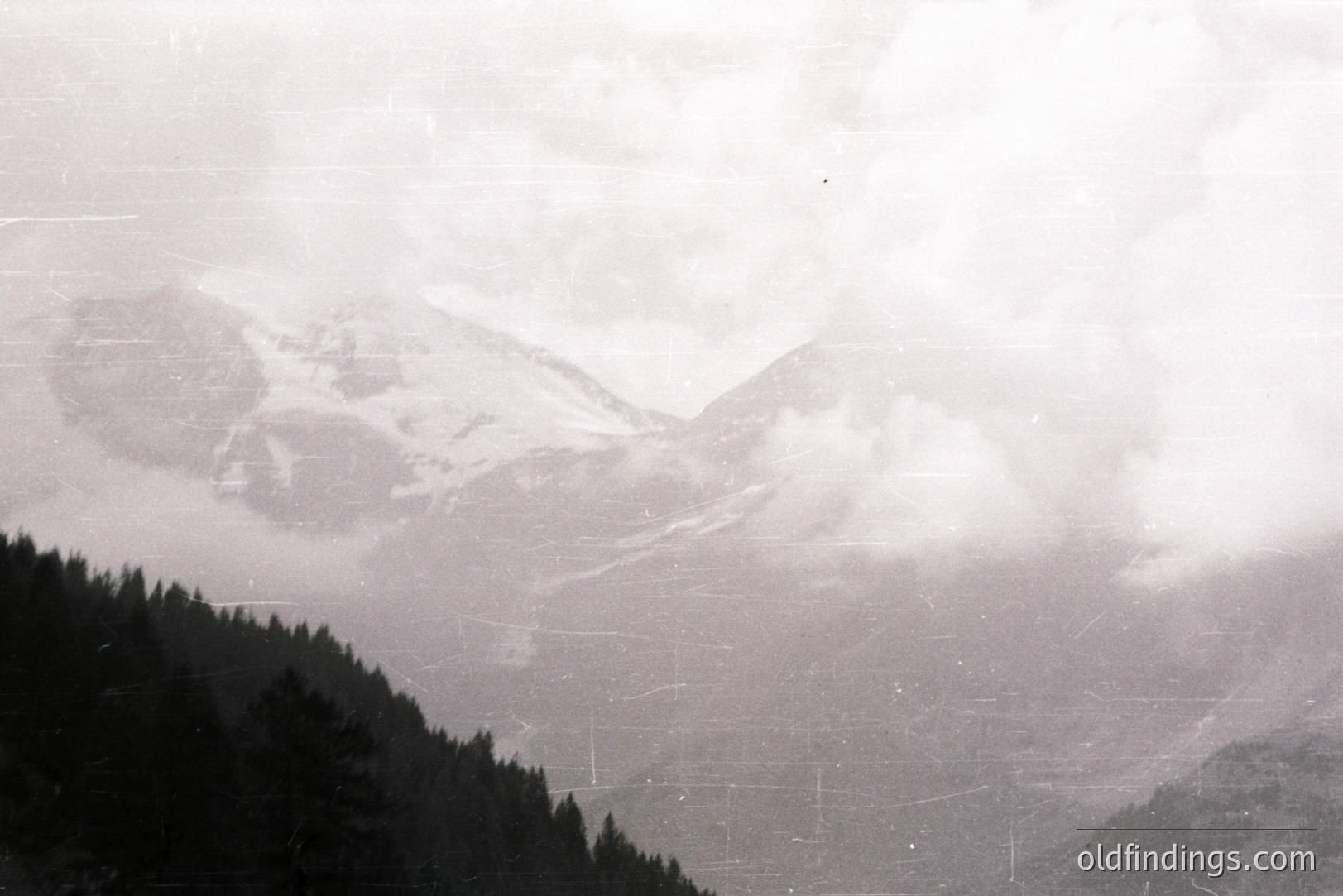 Monochrome landscape depicting a mountainous, forested region shrouded in mist and fog. Visible slopes suggest winter conditions with potential for skiing or recreation. A sense of scale conveyed through atmospheric perspective. Likely a 1960s or 70s amateur photograph.