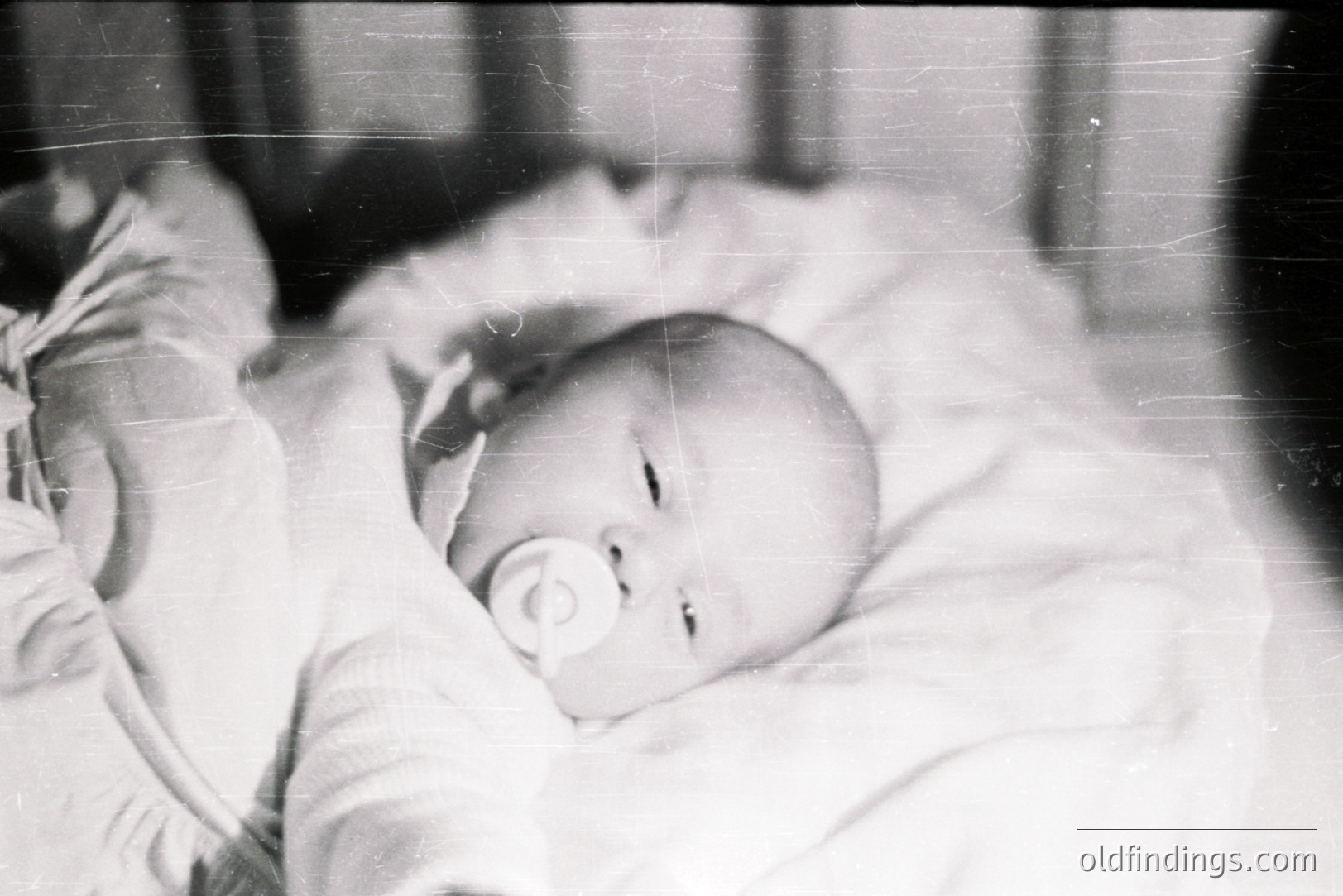 Infant lies asleep, pacifier in mouth, swaddled in a textured blanket. Appears to be a candid, intimate moment, likely a family snapshot. The black and white film and visible scratches suggest a mid-20th century origin, possibly 1950s-1970s. Valuable for archival or historical stock photography.