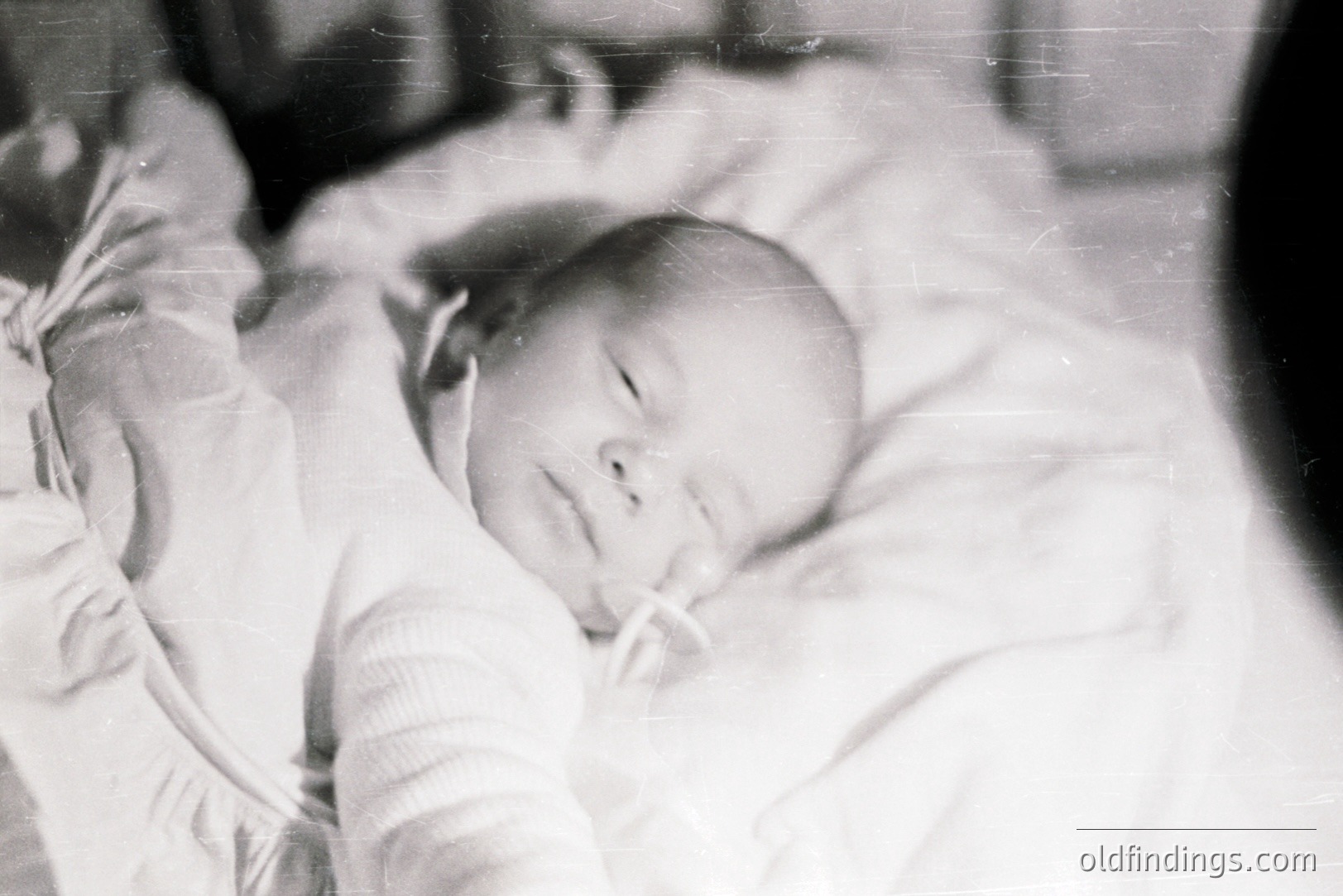 Close-up, monochrome portrait of a peacefully sleeping infant swaddled in soft fabric. The image exhibits characteristic grain and light falloff of mid-century photography, possibly 1950s-1970s. Strong potential for use in designs needing vintage baby imagery.