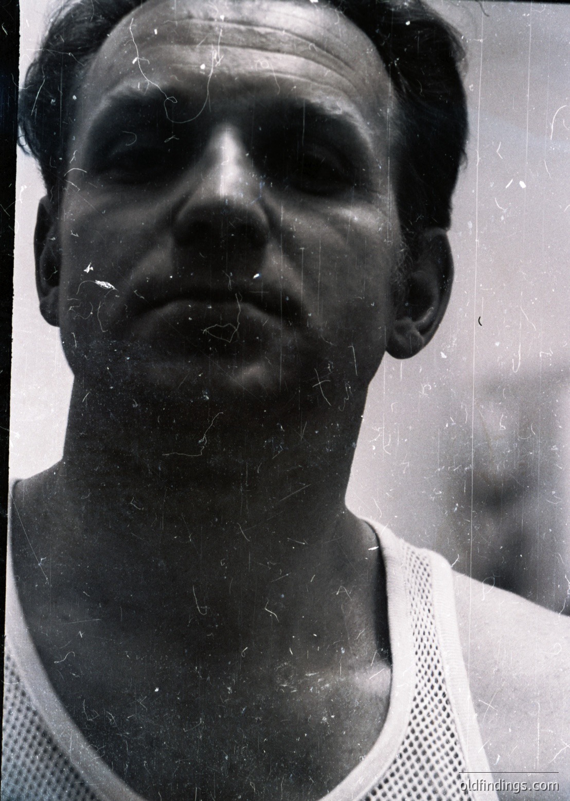 Vintage black-and-white portrait of a man in a mesh athletic jersey, likely from the 1960s–1970s. Close-up shot with visible scratches and wear on film, suggesting archival quality. Neutral expression, framed by blurred background.