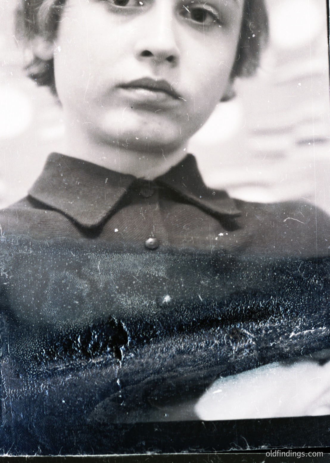 Portrait of a young individual in a dark, high-collared uniform, likely from the mid-20th century. The style suggests a school or youth organization setting, possibly Eastern Bloc-era. Noticeable wear on the photo edges indicates age and handling. [mid20thcenturypic ]