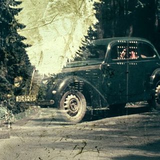 Vintage car driving through dense forest.