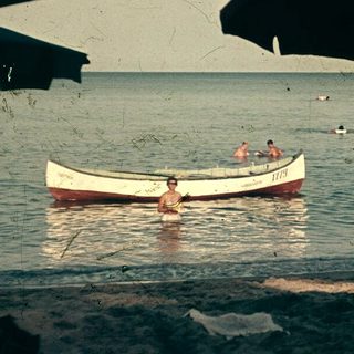 Beach scene with people swimming, boat, and shaded seating area.