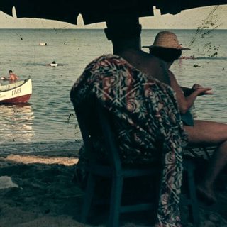 Beach scene with people swimming, boat, and shaded seating area.