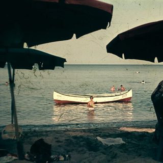 Beach scene with people swimming, boat, and shaded seating area.