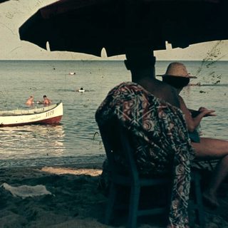Beach scene with people swimming, boat, and shaded seating area.