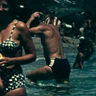 Vintage beach scene with people swimming and boating.