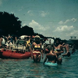 Vintage beach scene with people swimming and boating.
