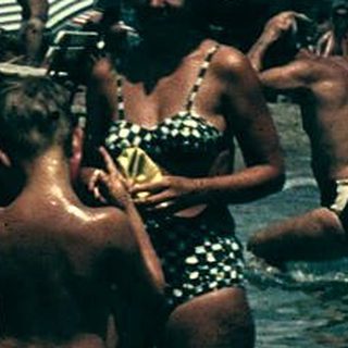 Vintage beach scene with people swimming and boating.