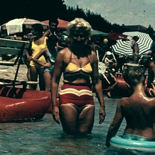 Vintage beach scene with people swimming and boating.