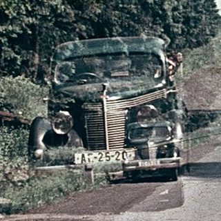 Vintage car driving through forested road.