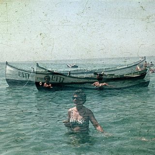 Vintage seaside scene with people swimming and boating.