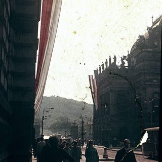 Vintage street scene with flags, historic architecture, pedestrians.