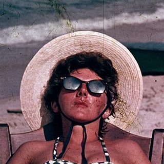 Woman relaxing on beach in checkered swimsuit and hat.