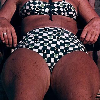 Woman relaxing on beach in checkered swimsuit and hat.