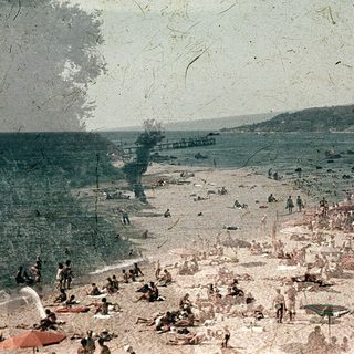 Busy beach scene with people sunbathing and swimming.