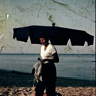 Woman holding umbrella on beach with towel.