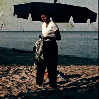 Woman holding umbrella on beach with towel.