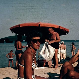 Sunbathing men at beach with umbrellas, mid-20th century.