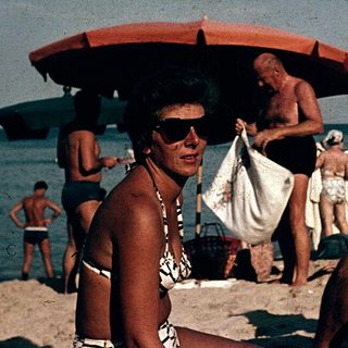Sunbathing men at beach with umbrellas, mid-20th century.