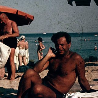 Sunbathing men at beach with umbrellas, mid-20th century.
