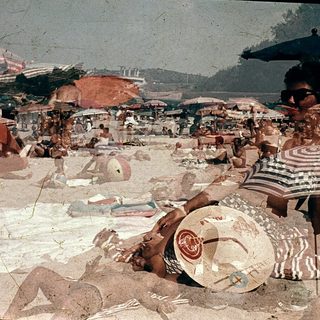 Busy beach scene with people relaxing under umbrellas.