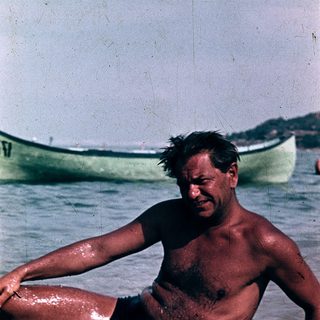Shirtless man sitting in shallow ocean water.