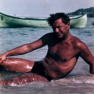 Shirtless man sitting in shallow ocean water.