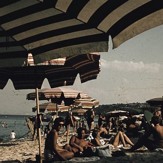 Beach scene with people relaxing under striped umbrellas.