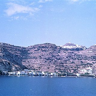 Coastal village nestled by calm sea with hilly terrain.