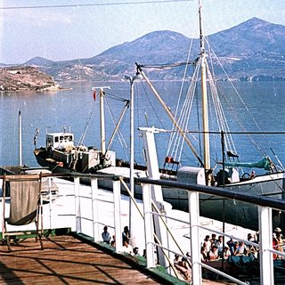 Ferry docked near mountainous coastline with passengers.