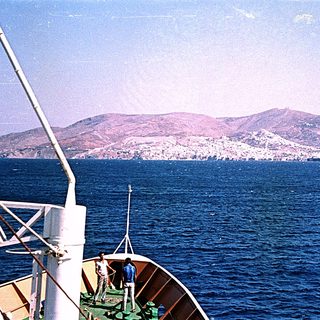 Boat on sea with coastal city and hills.