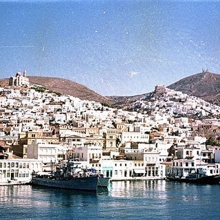 Coastal town with white buildings, harbor, and hilltop fortress.