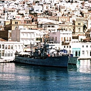 Coastal town with white buildings, harbor, and hilltop fortress.