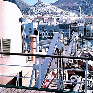 Ship deck view of coastal city with historic fortress on hill.