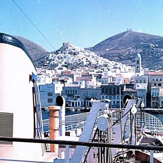 Ship deck view of coastal city with historic fortress on hill.